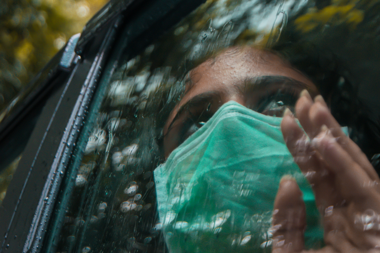 Adolescente usando máscara facial, olhando pela janela de um carro em um dia chuvoso.