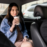 Passageira sentada no banco traseiro de um carro tomando café durante trajeto urbano.