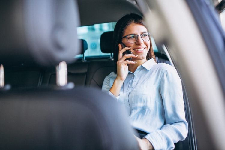 Mulher sorrindo e falando ao celular no banco traseiro de um carro.