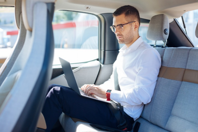 Profissional usando notebook no banco traseiro de um carro durante um deslocamento corporativo.